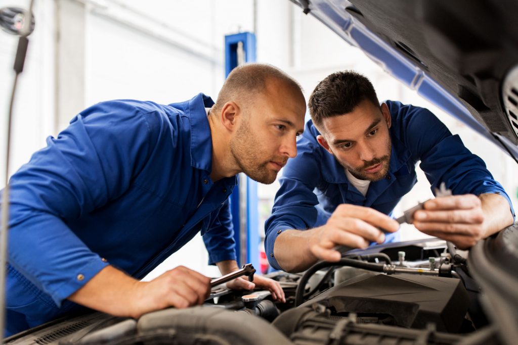 auto service, repair, maintenance and people concept - mechanic men with wrench repairing car at workshop