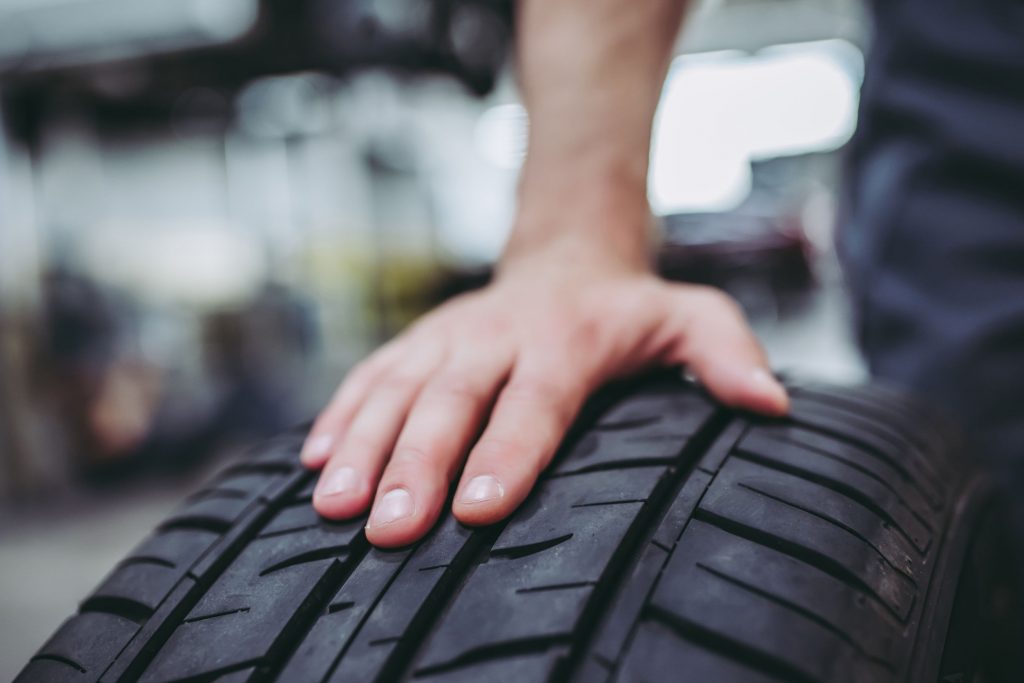 Cropped image of handsome mechanic in uniform is working in auto service. Car repair and maintenance. Holding car wheel/tire.